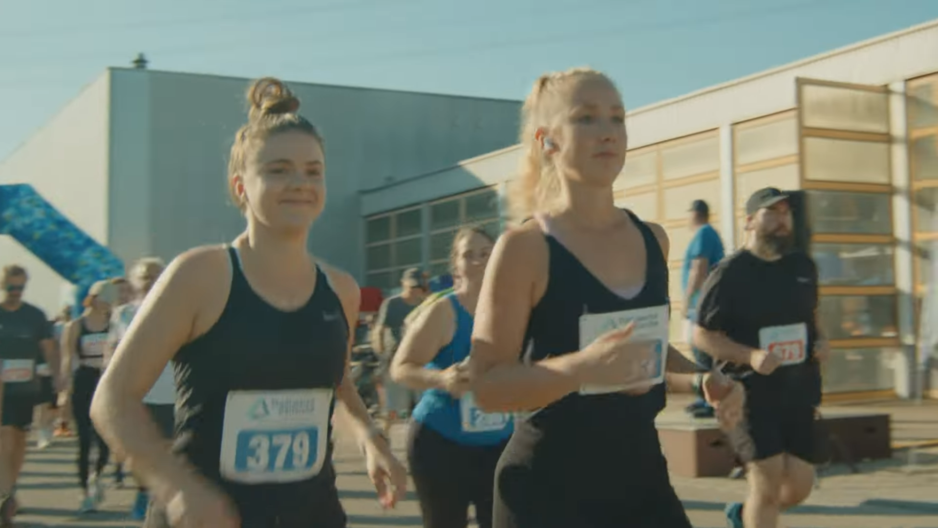 Zwei Frauen laufen bei sonnigem Wetter energiegeladen einen Volkslauf, Startnummern sichtbar. Eine lebendige Aufnahme des Sportereignisses der Stadtwerke Karlsruhe.
