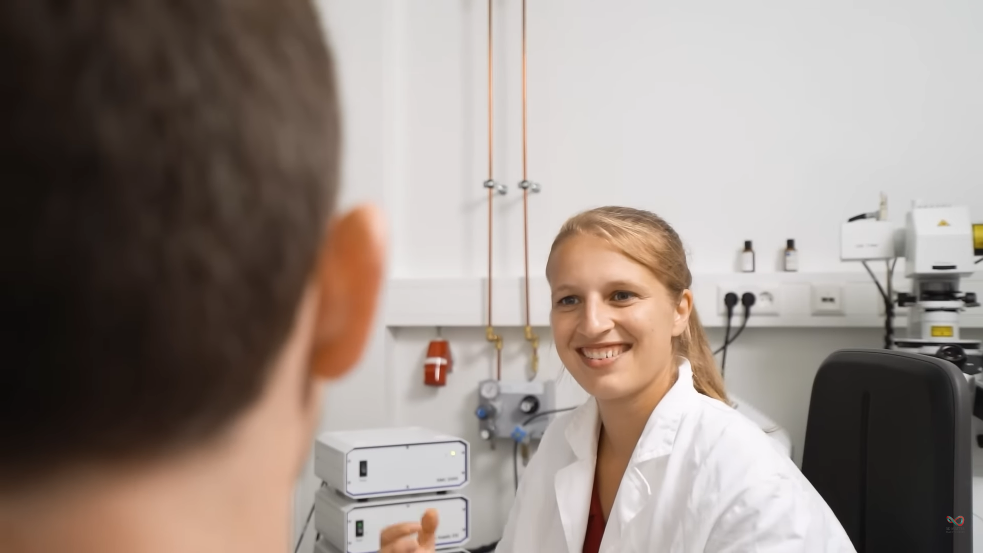 Lächelnde Wissenschaftlerin in Laborkittel in einem hellen Forschungslabor, passend zu den 'Women in Science'-Videos für 3DMM2O.