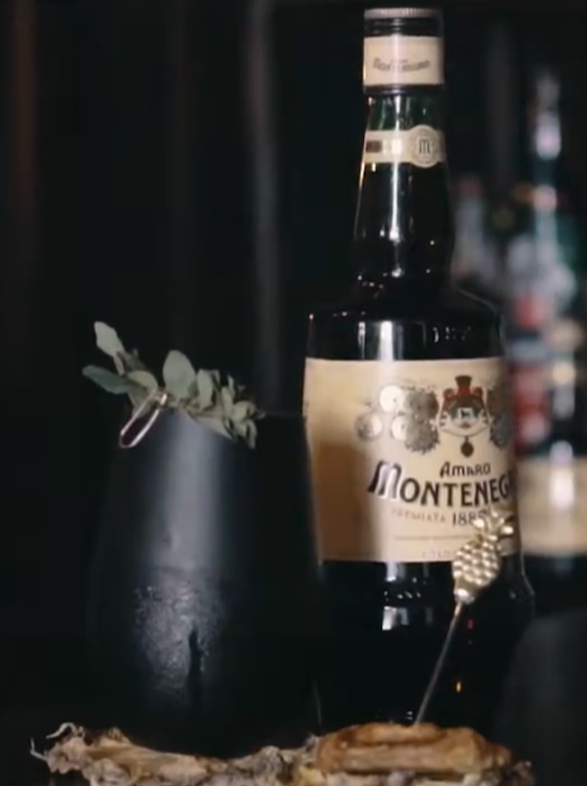 Amaro Montenegro Flasche und ein elegant garnierter Cocktail in dunkler, stimmungsvoller Bartender-Szene.