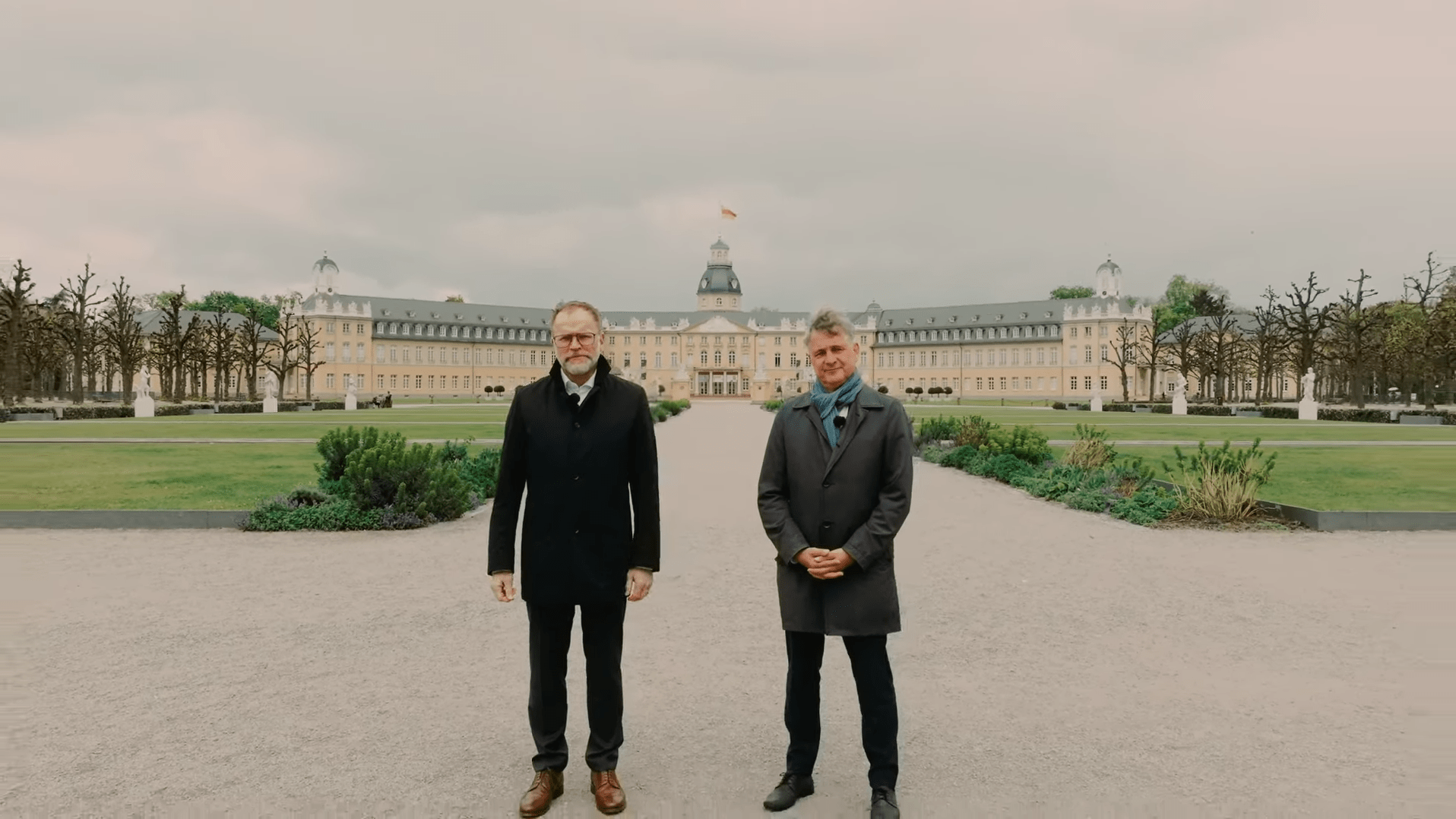 Oberbürgermeister und Geschäftsführer der Stadtwerke Karlsruhe vor dem Karlsruher Schloss in einem Videostill.