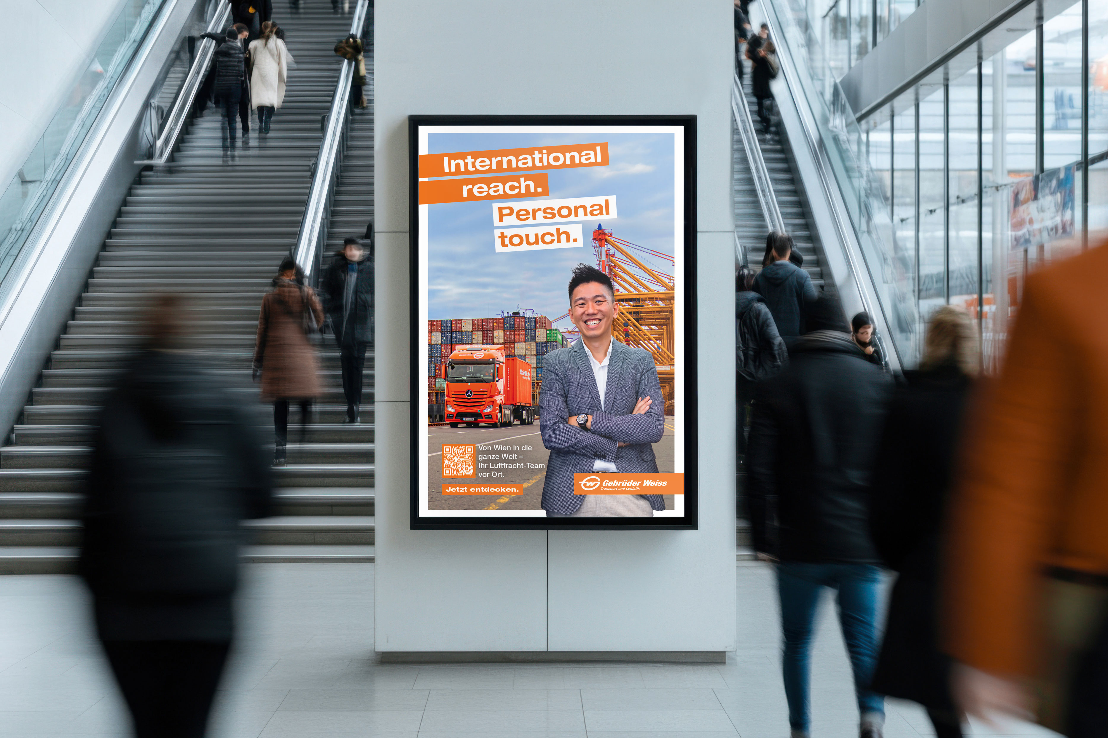 Ein Plakat mit dem Schriftzug "International reach. Personal touch." der Gebrüder Weiss hängt im urbanen Raum.