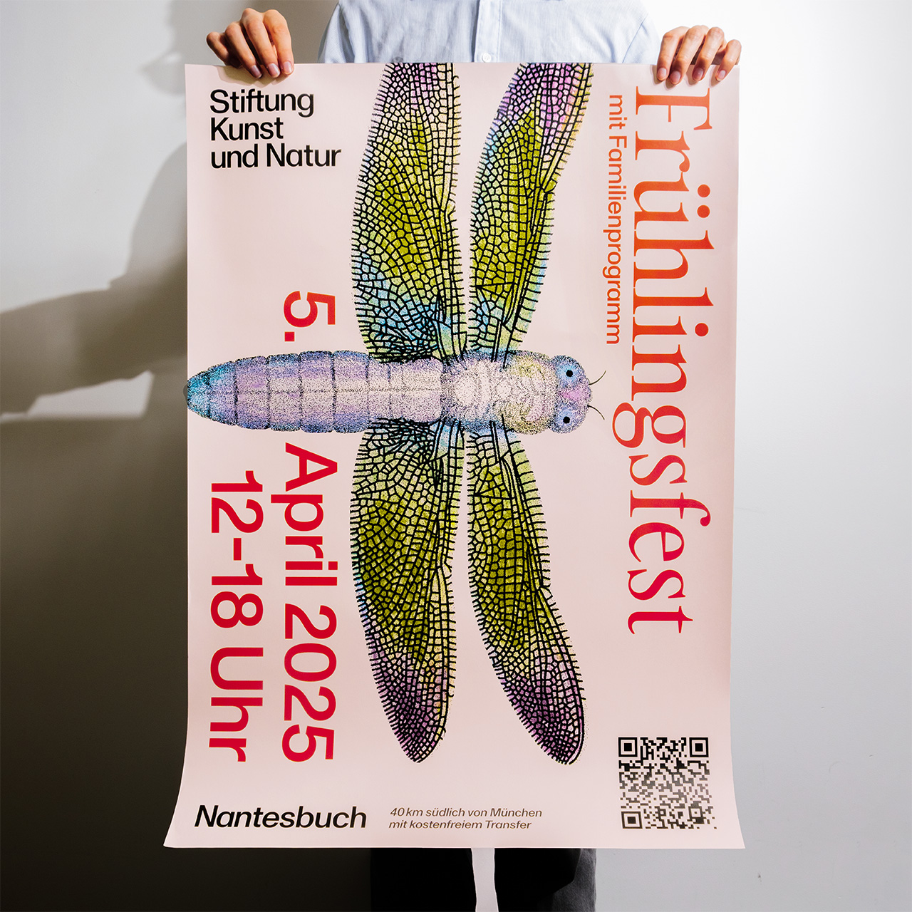 Eine Person hält das farbenfrohe Plakat mit einer Libelle der "Stiftung Kunst und Natur" für deren Frühlingsfest