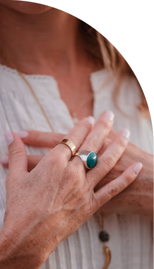 Close-up of an older person’s hands with rings resting on their chest over a white blouse.