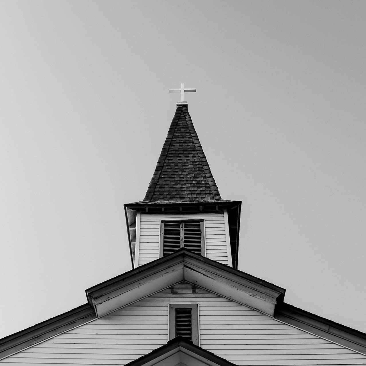 An old-time church with a steeple, taken from outside the front door, looking straight up the building. Taken in black-and-white.