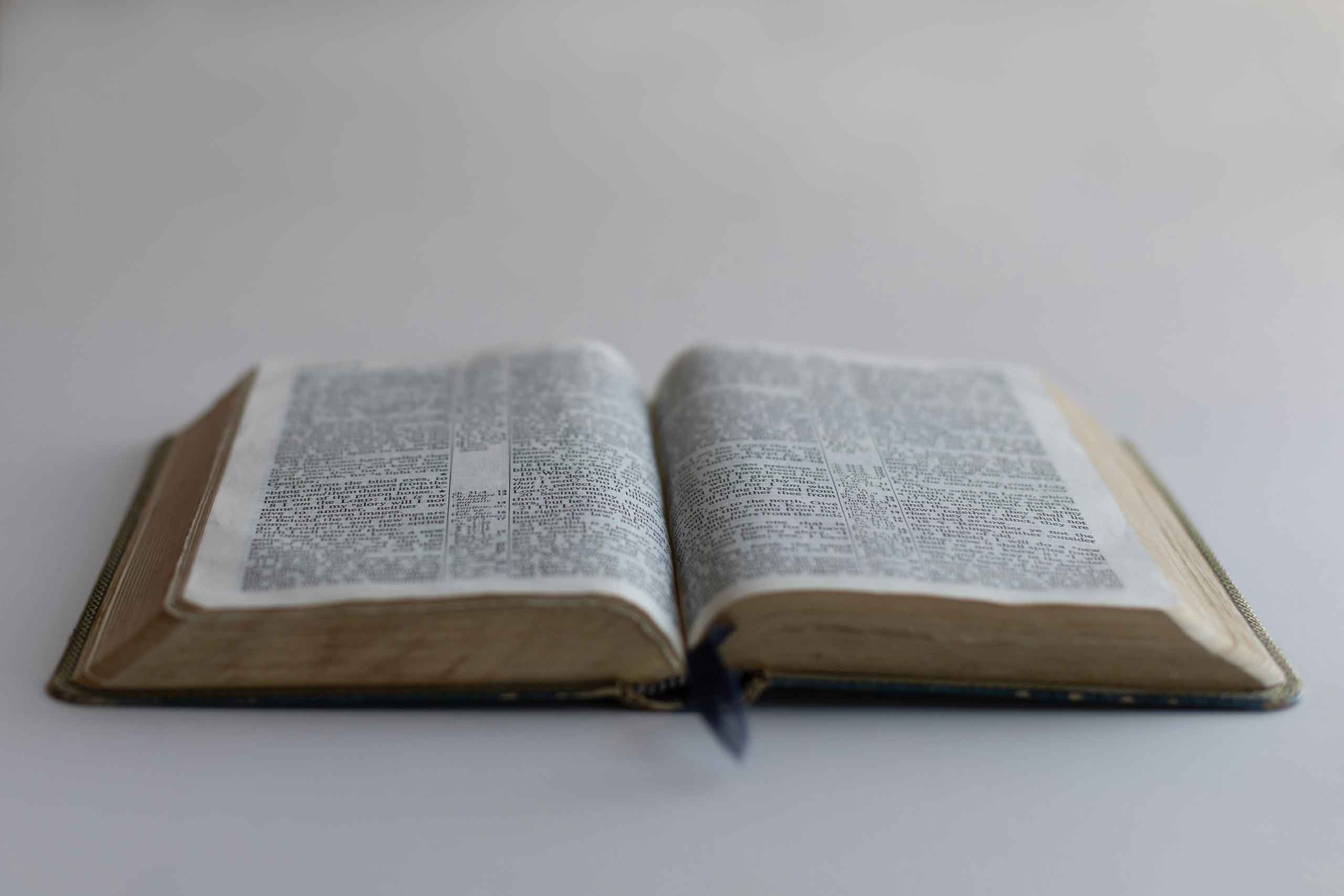 Bible laying flat on completely white background with a subtle gradient to it, taken from a 45 degree angle towards the bottom of the Bible.