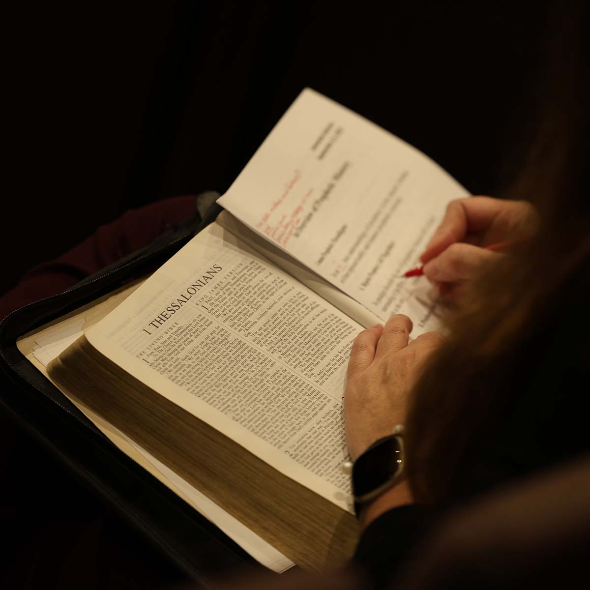A student studying Scripture with Bible open in lap. Photo taken from behind left shoulder, looking into lap.