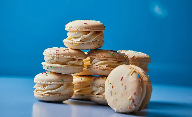 Stack of colorful macarons with yellow filling on blue background