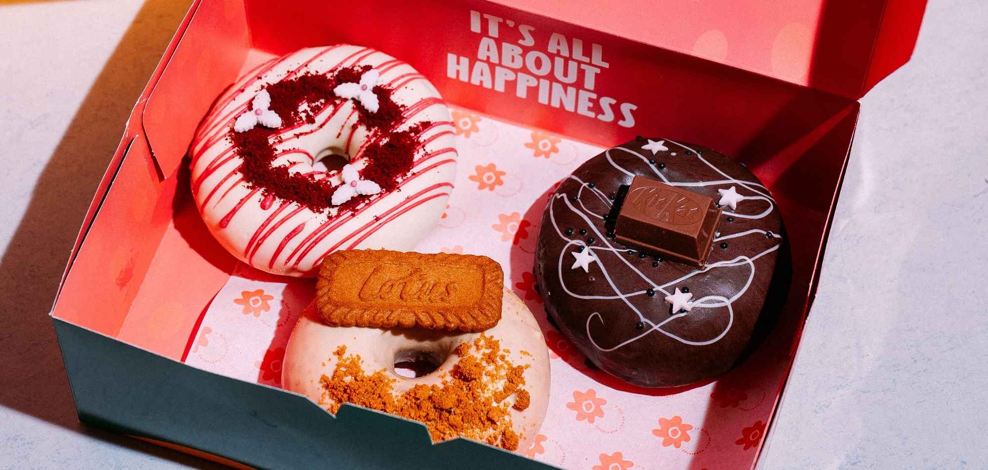 Red gift box containing four decorated donuts with sprinkles and toppings inside