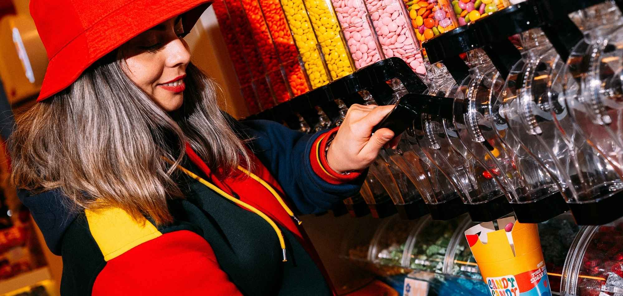 Woman in red hat selecting colorful candy from bins at candy store display