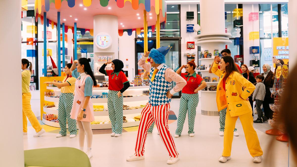 Colorful performers in costume dancing in a vibrant toy store with festive decorations.