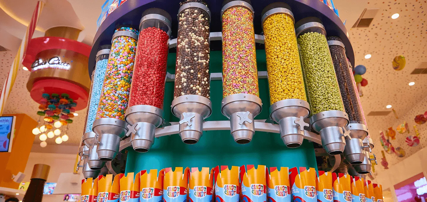 Colorful candy dispensers with various candies in glass tubes mounted on display stand.
