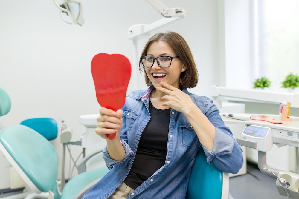 A woman sitting in a dentist chair holding a red mirror.