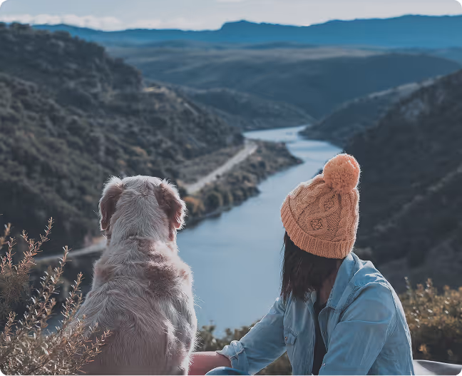 A woman sitting next to a dog on top of a hill.