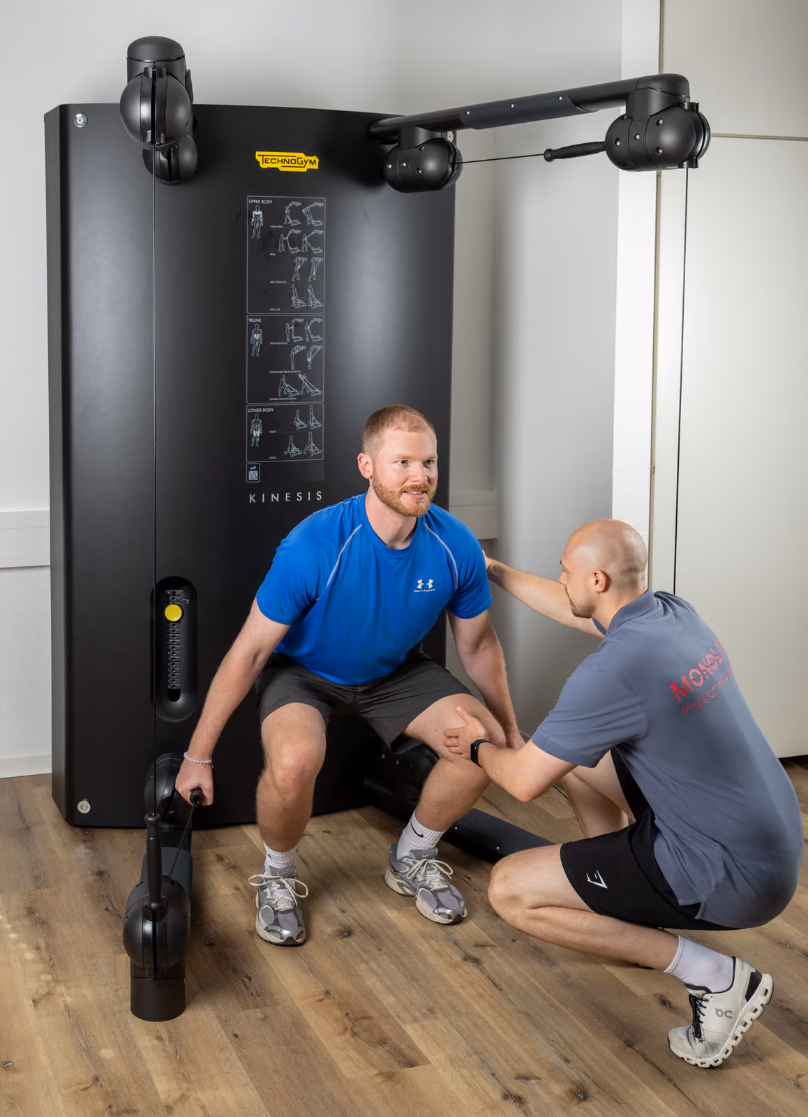 Physiotherapeut unterstützt Mann bei Übung an Technogym Kinesis Trainingsgerät.