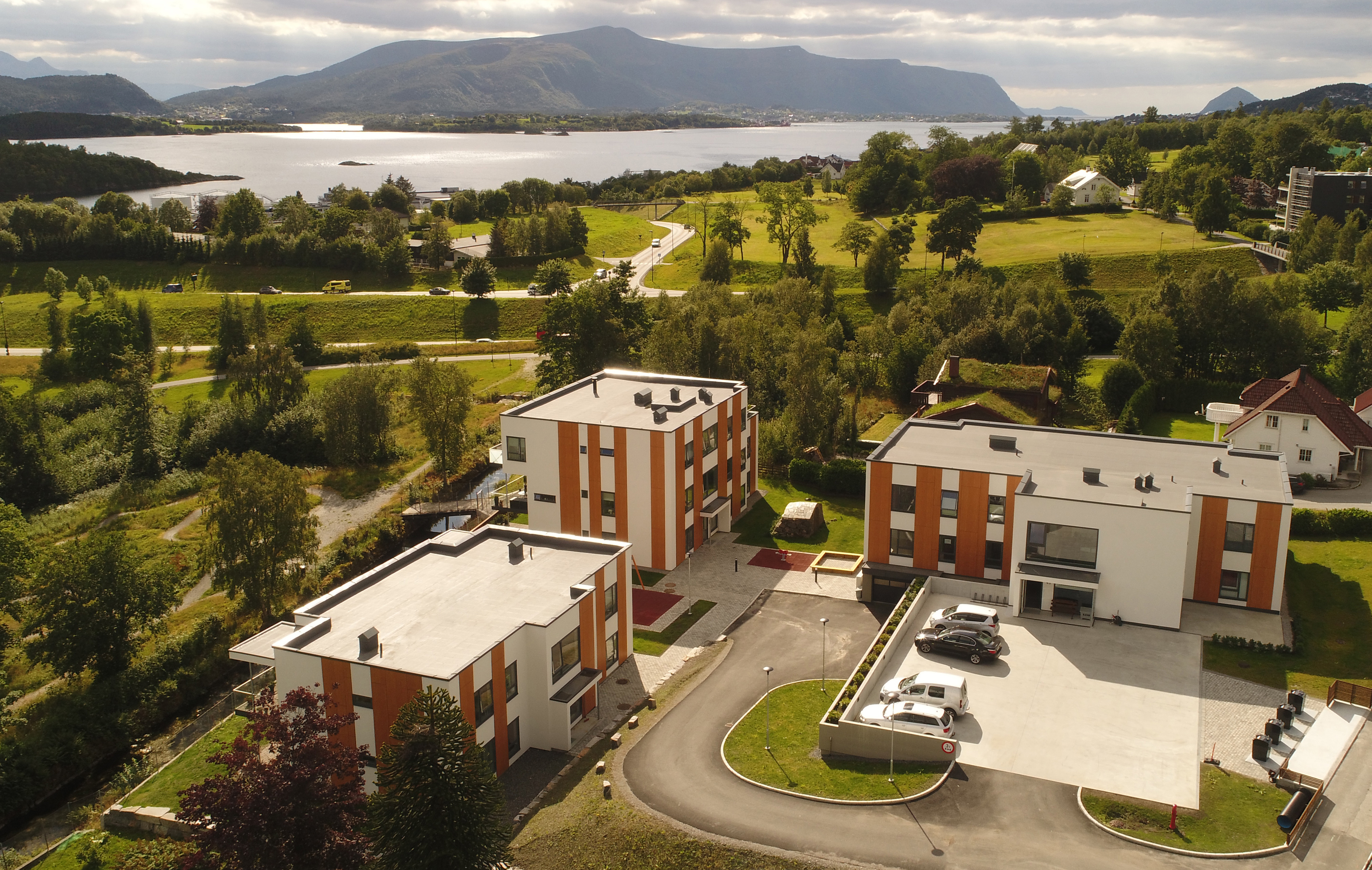 Visualisering av boligområde med moderne rekkehus i tre, grønne fellesarealer og små gangveier mellom enhetene.