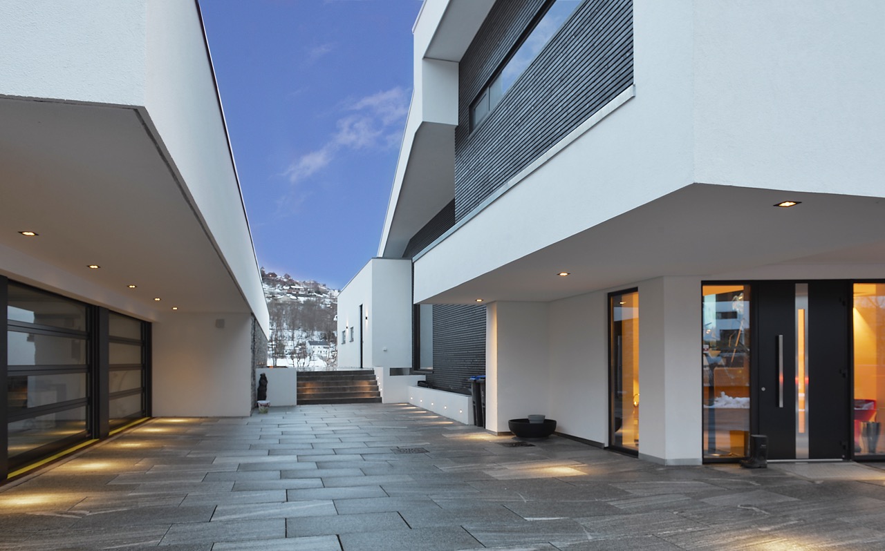 Inngangsparti og gårdsrom i minimalistisk betong- og pussutførelse, med uplights og rene linjer i arkitekturen.