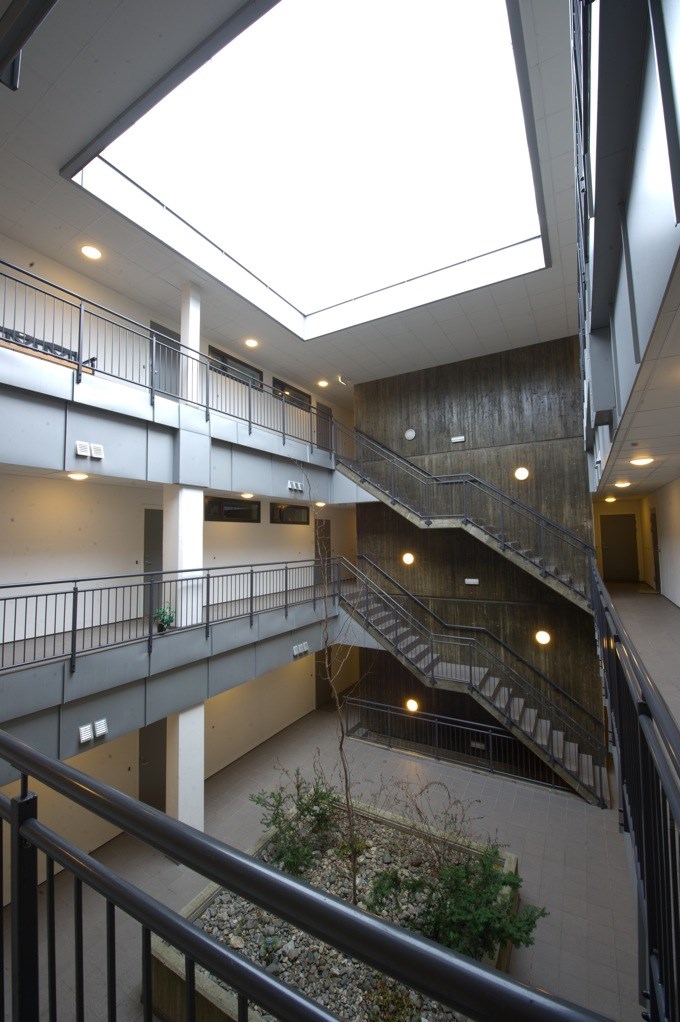 Interiørbilde av fellesareal med åpen himling, trappeløp og plantebed i midten av byggets atrium.