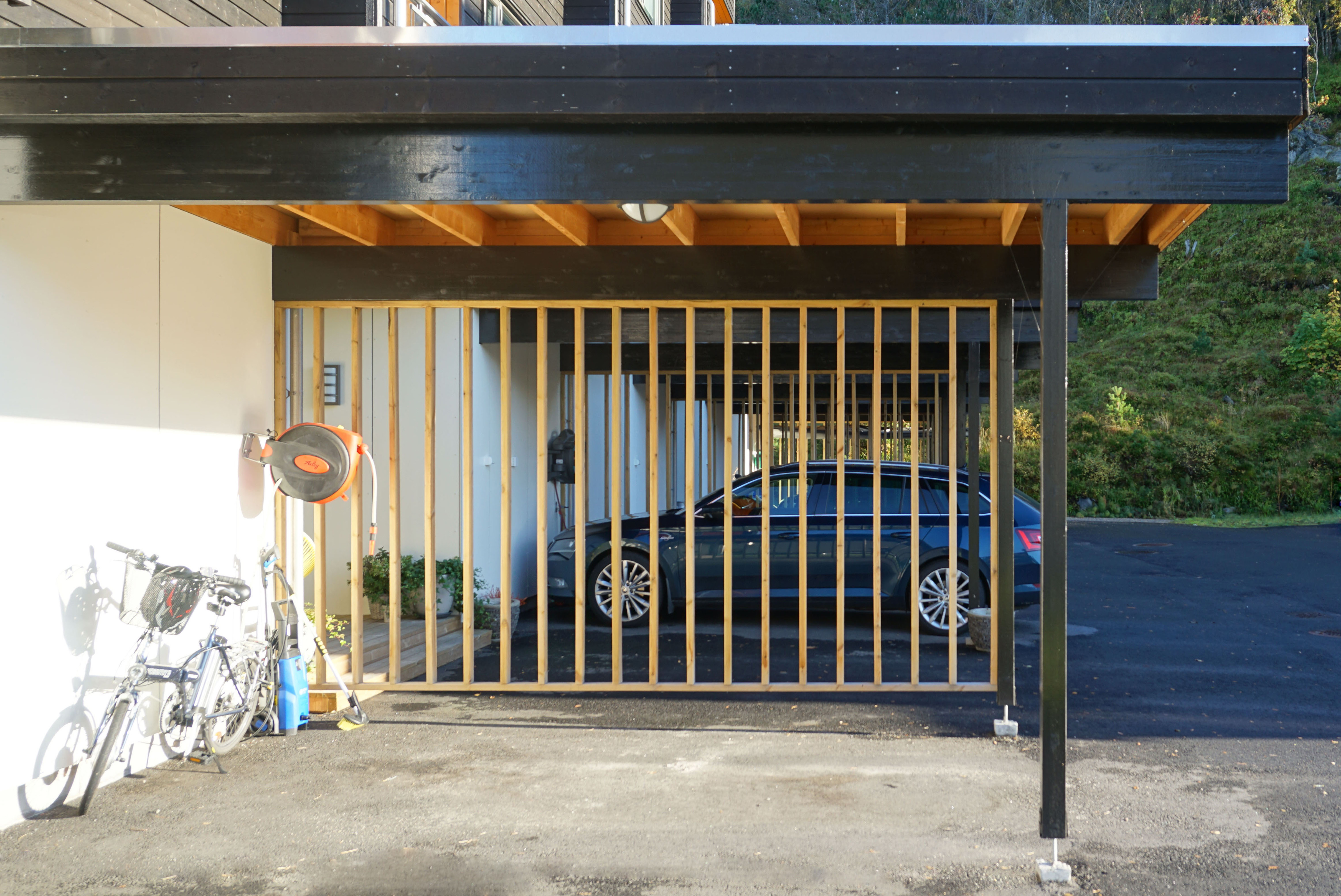 Detalj av carport med trekonstruksjon og sykkeloppbevaring, sett fra gårdsrom.