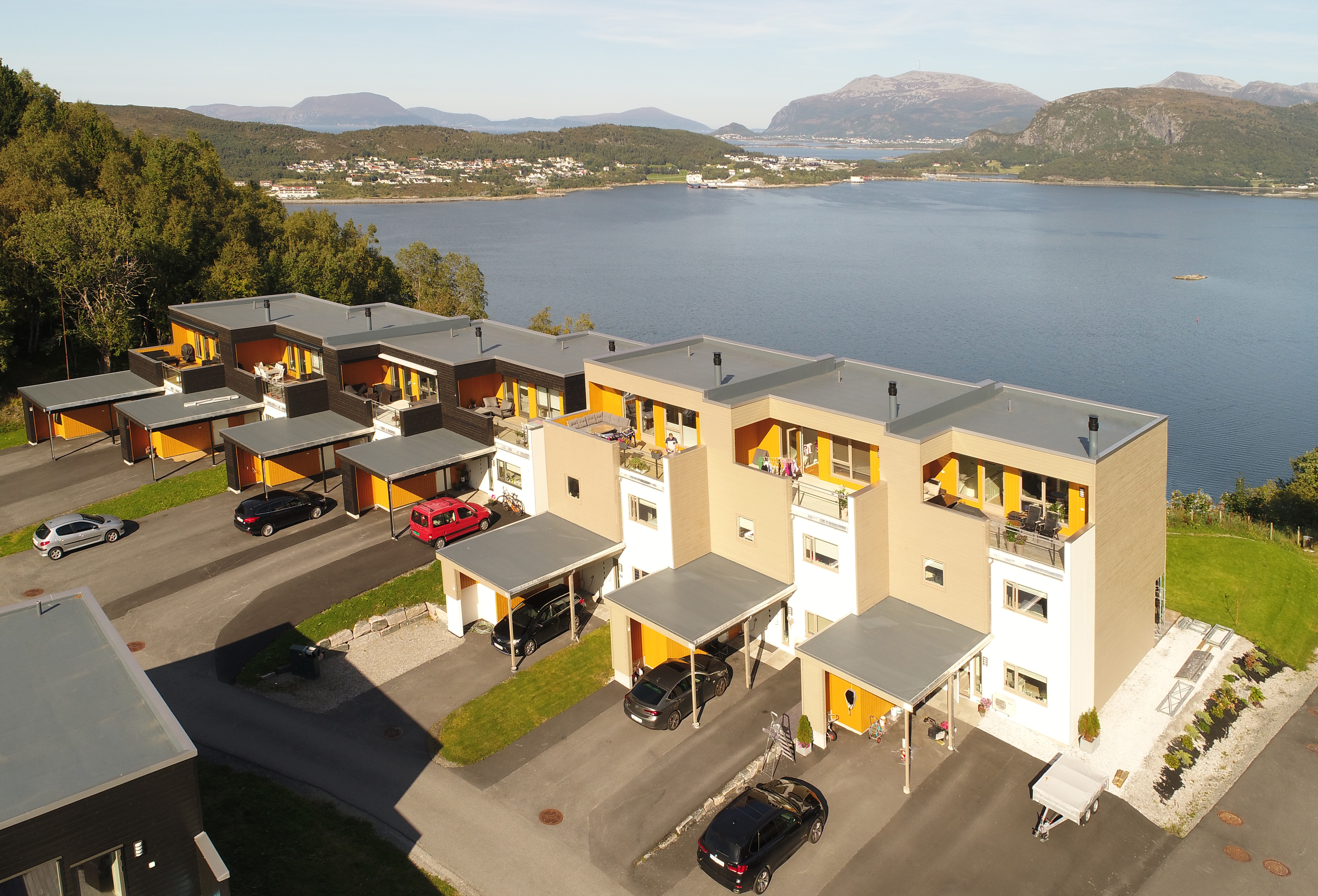 Luftperspektiv av boligfeltet med fjordutsikt, rekkehus i ulike farger og fellesveier mellom byggene.