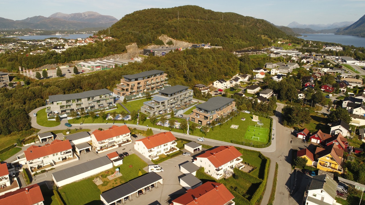 Visualisering av nytt boligprosjekt med flere leilighetsbygg i grønne omgivelser nær bysenter og sjø.