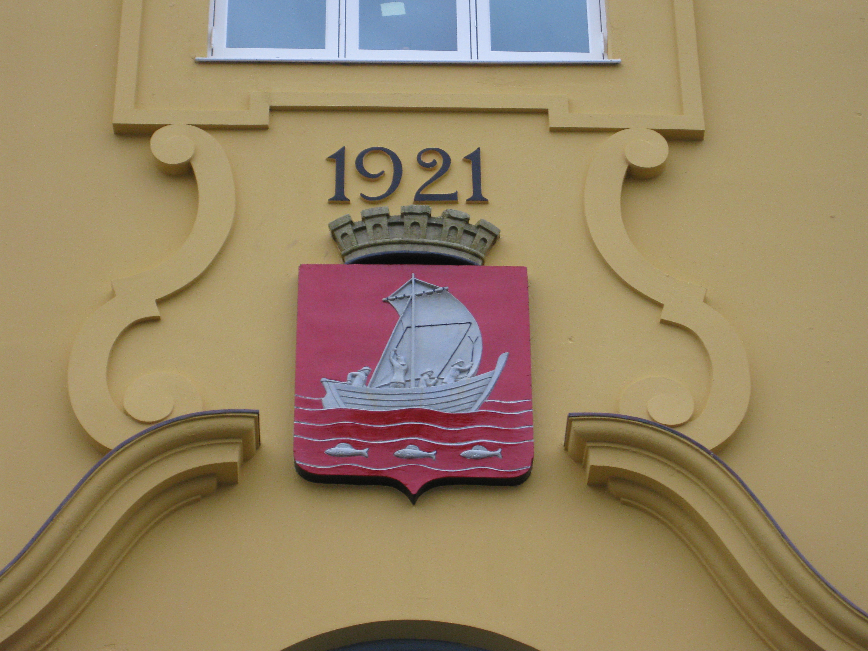 Nærbilde av kommunevåpen og årstallet 1921 over hovedinngangen til bygget.