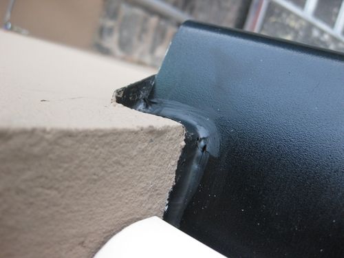 Detalj av beslag i underkant av vindu, tett inntil pussfasade.