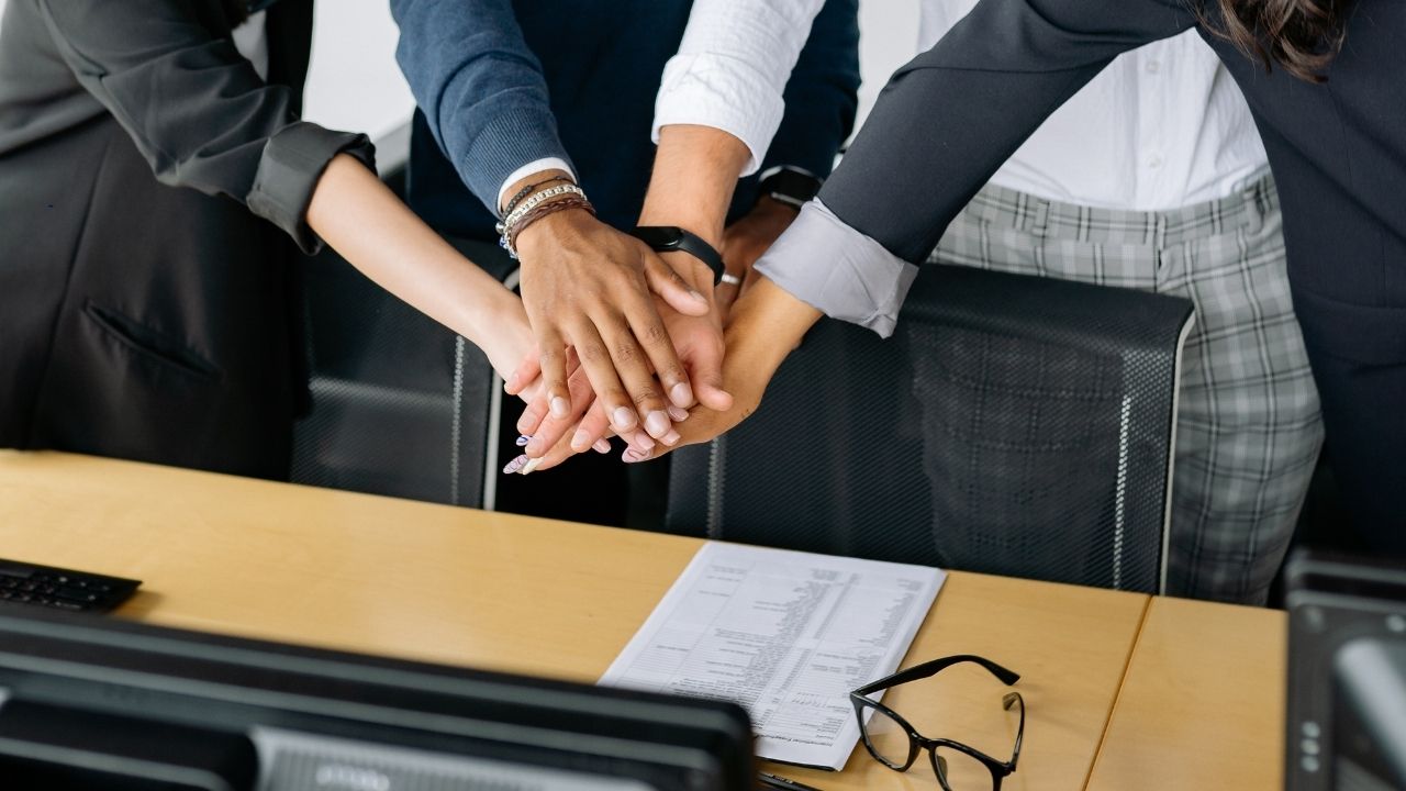 Ein TEam legt die Hände zusammen, um Zusammenarbeit, Zusammenhalt zu symbolisieren.