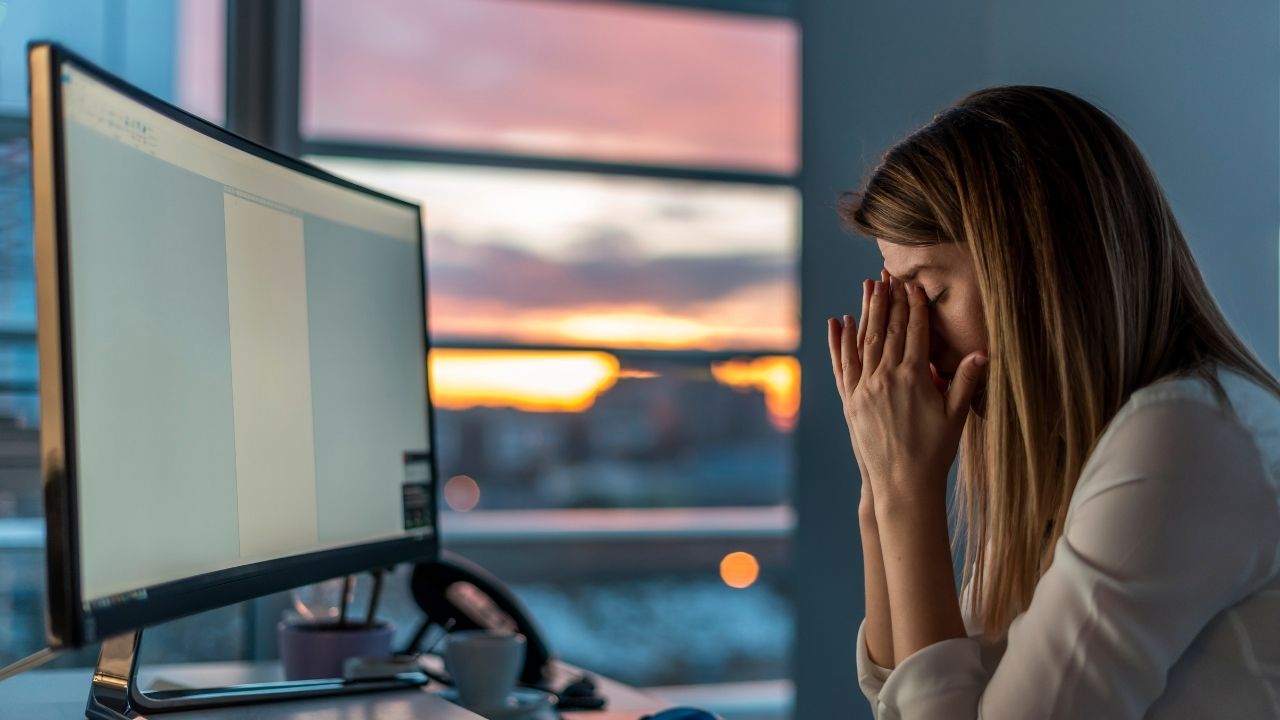 Geschäftsfrau sitzt vor dem Computer mit Händen am Kopf, wirkt gestresst und blockiert-Innovationsstau, keine kreativen Ideen möglich. Entstehung durch Chaos und hohe Entropie, kreative Blockade im Arbeitsumfeld.