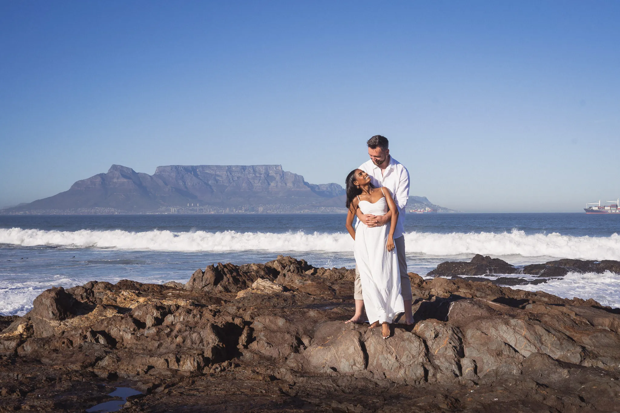Couple standing on rocks at Bloubergstrand with Table Mountain behind — couple photographer Cape Town