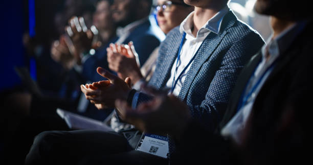 Audience members in business attire clapping at an indoor event.