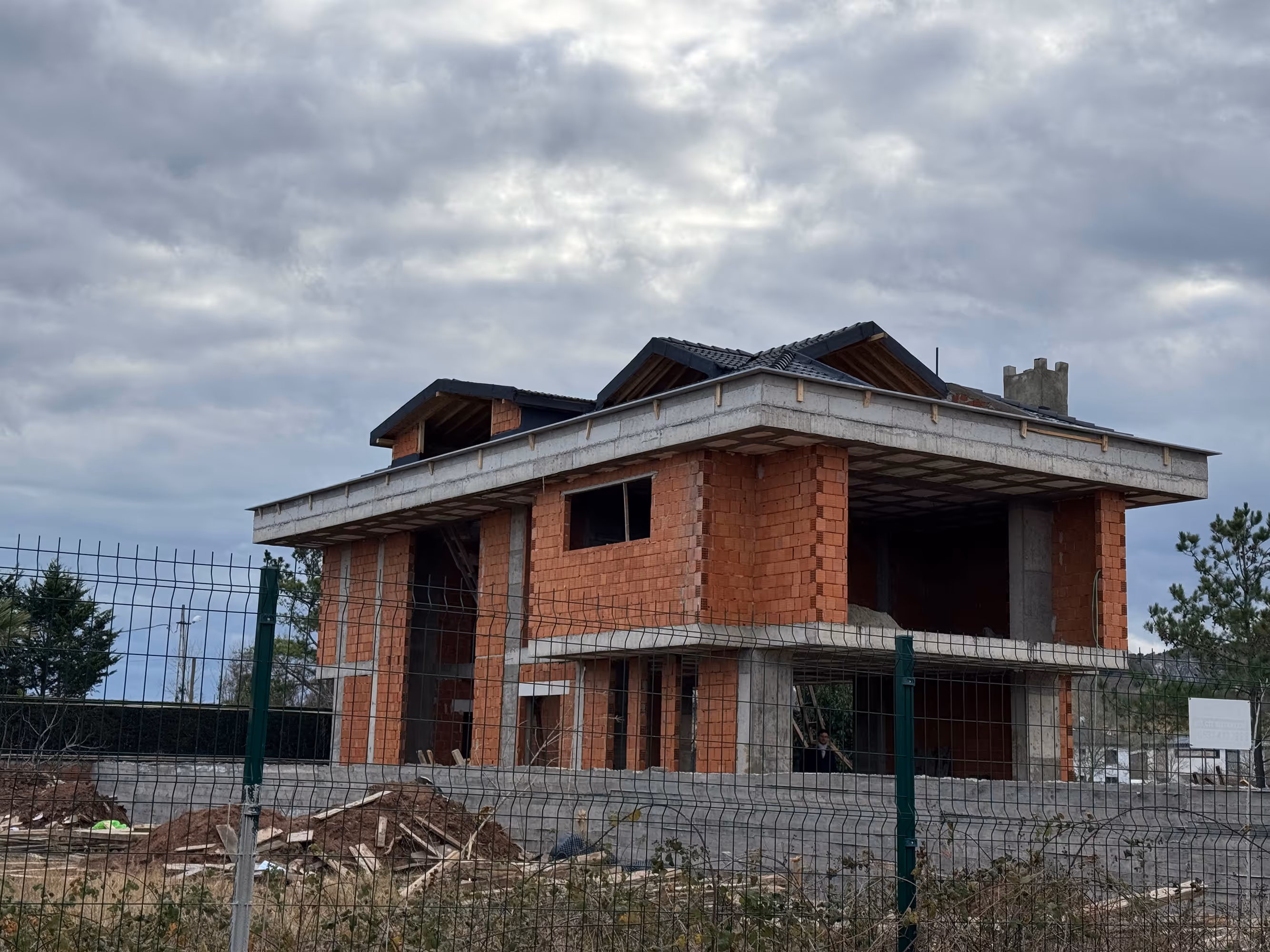 Contemporary two-story house with dark exterior panels and wooden accents, featuring a sloped roof, private pool, sun loungers, and outdoor seating area with barbecue in lush green surroundings.