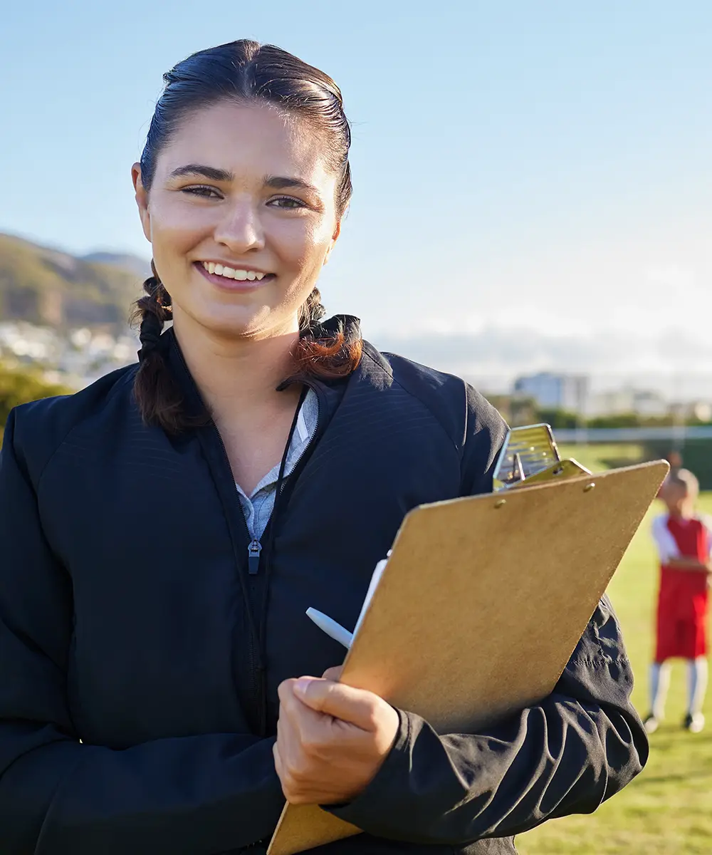 A female soccer coach smiling with soccer players in the background