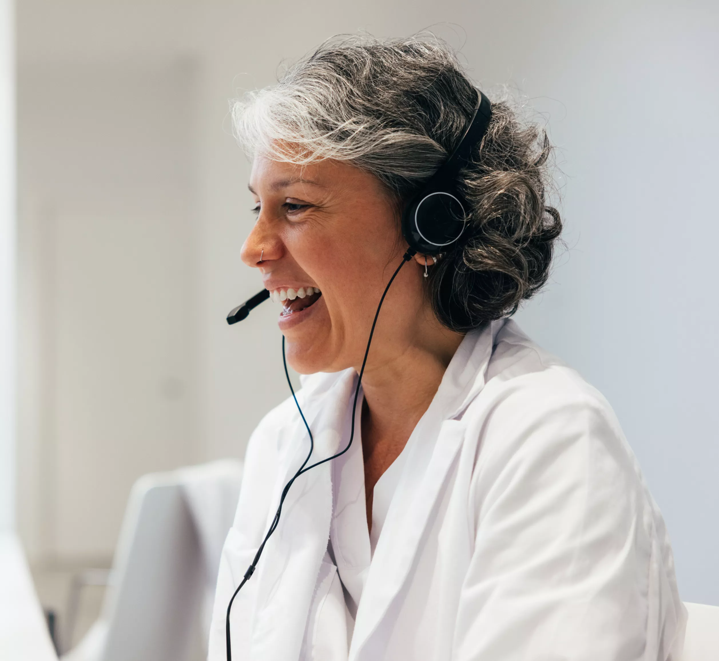 A smiling middle-aged woman wearing a lab coat and a headset