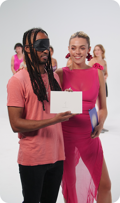 Man blindfolded holding a card while woman smiles beside him during Love at First Sign dating event.