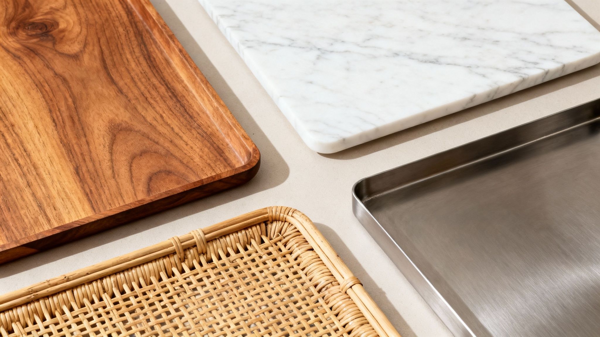 A close-up of four different textured serving trays: wood, marble, metal, and woven rattan.