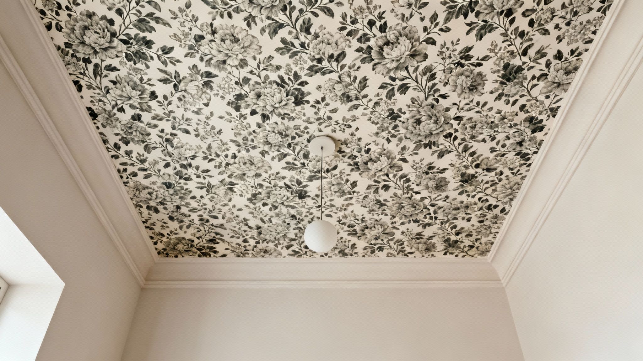 A chic ceiling features black and white floral wallpaper, white crown molding, and a modern pendant light.