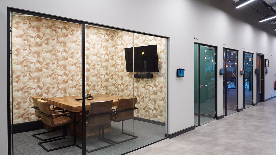 Modern office hallway with four glass-door meeting rooms and a visible room with wooden table and brown chairs.