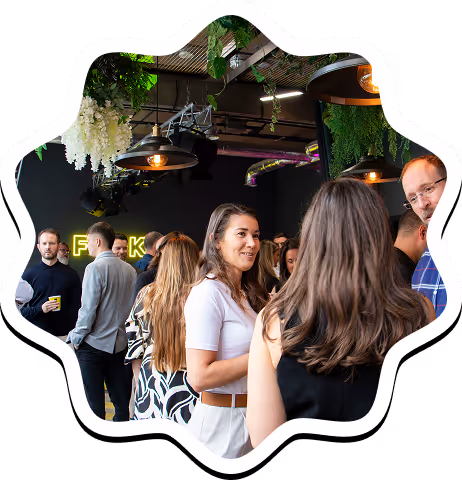 People socializing inside a modern event space with hanging plants and stylish lighting.