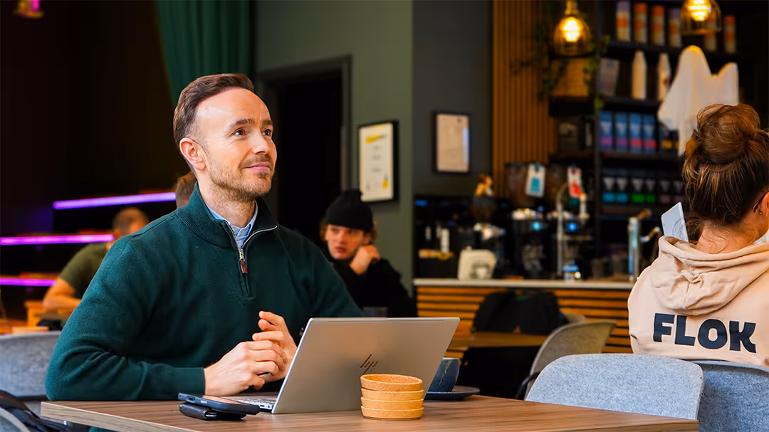 Man in green sweater sitting at table with laptop in Flok Cafe Area
