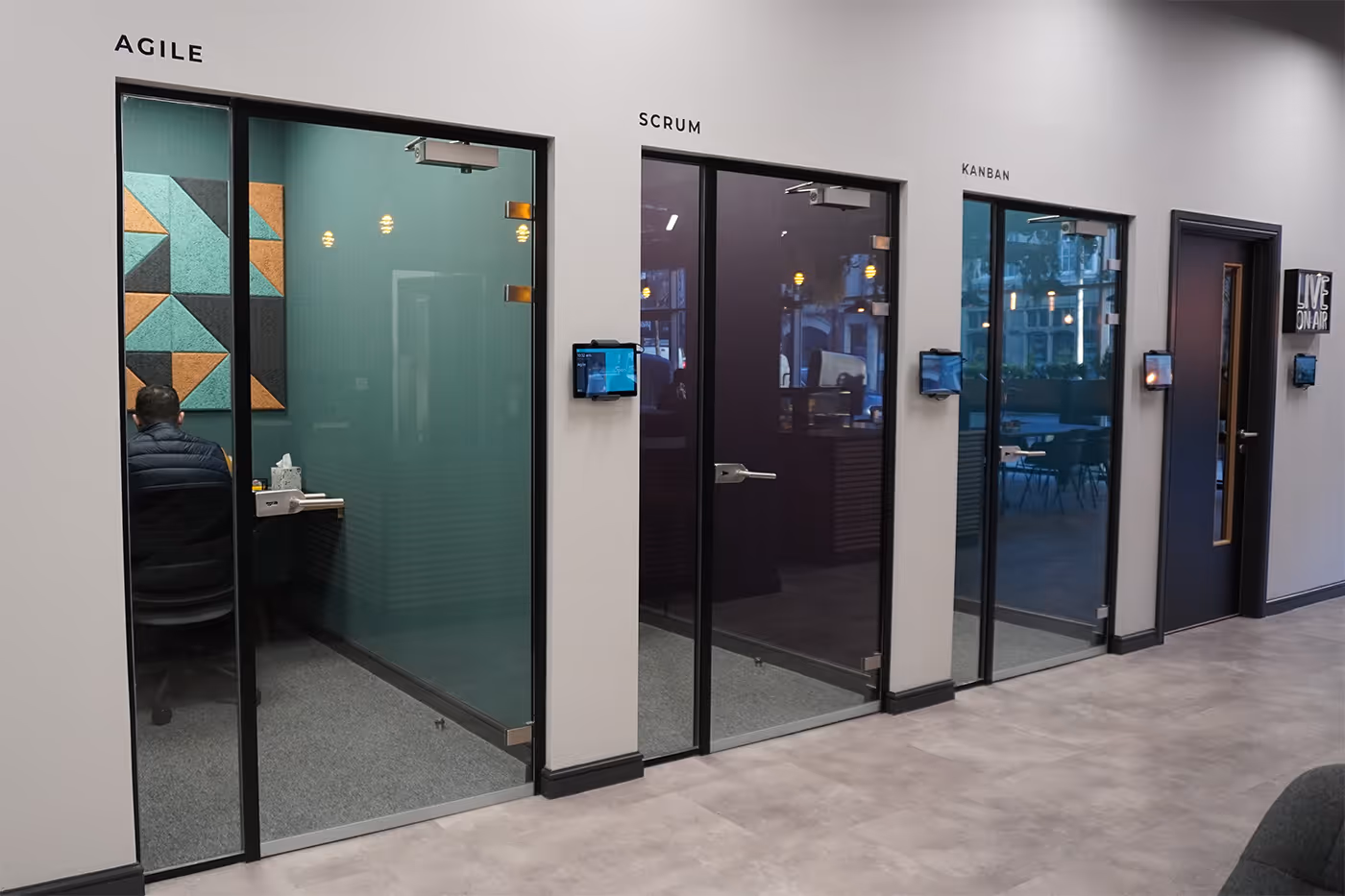 Three glass meeting rooms labeled Agile, Scrum, and Kanban with one person inside the Agile room.
