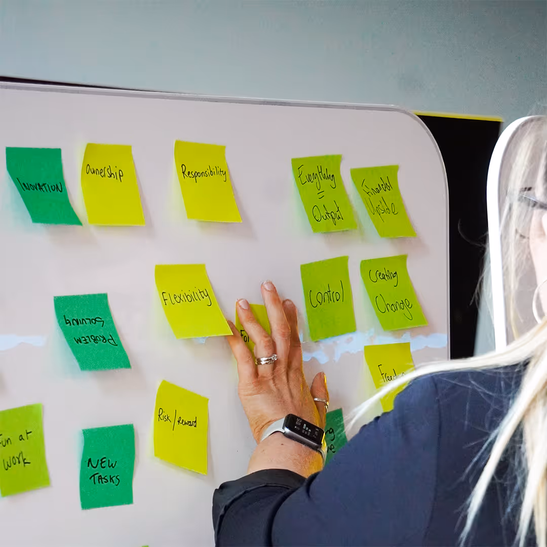 Person arranging sticky notes with words like Innovation, Ownership, Flexibility on a whiteboard.