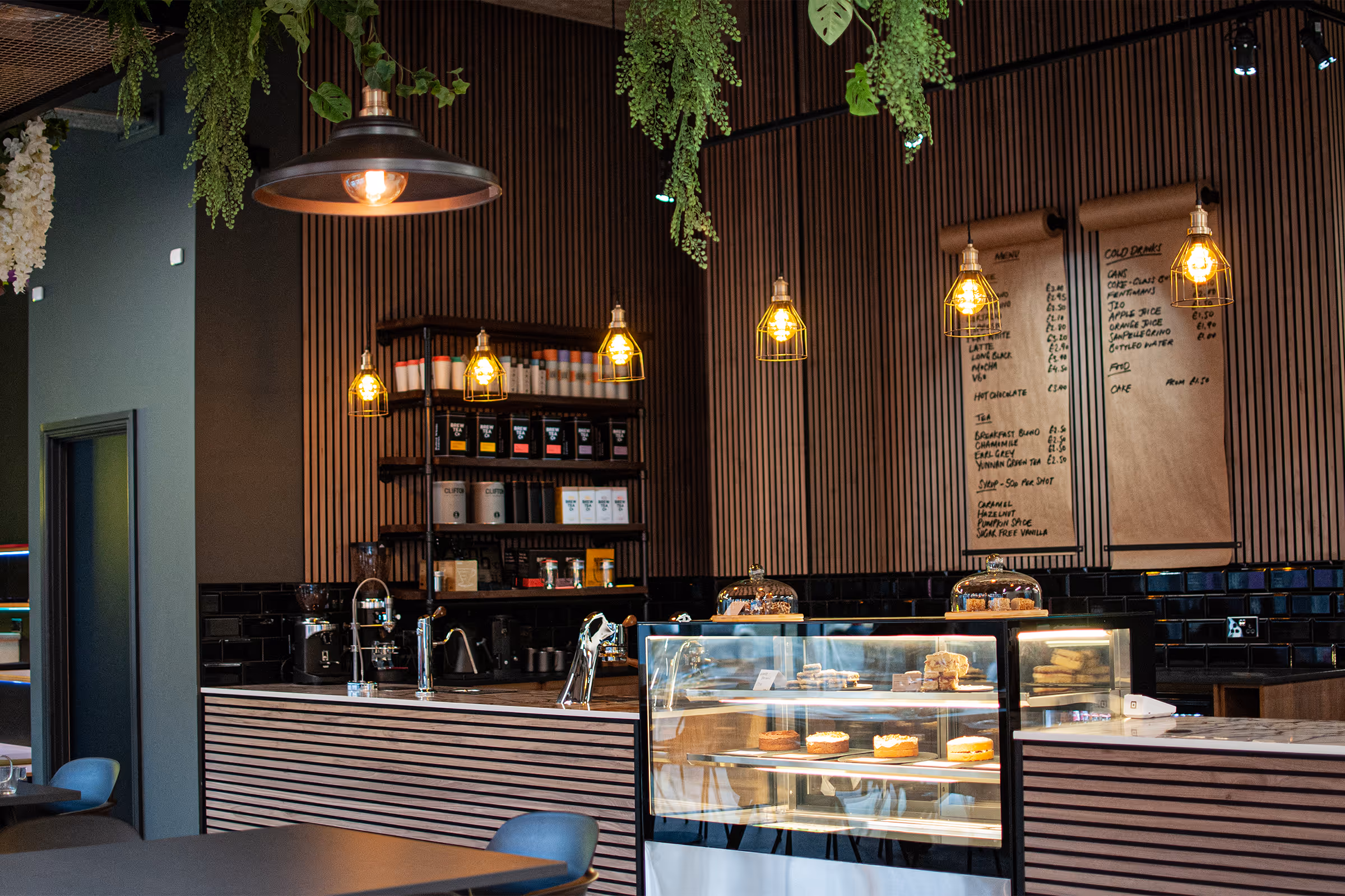 Modern coffee bar with hanging lights, a display case of pastries, and a menu on wood-paneled wall.