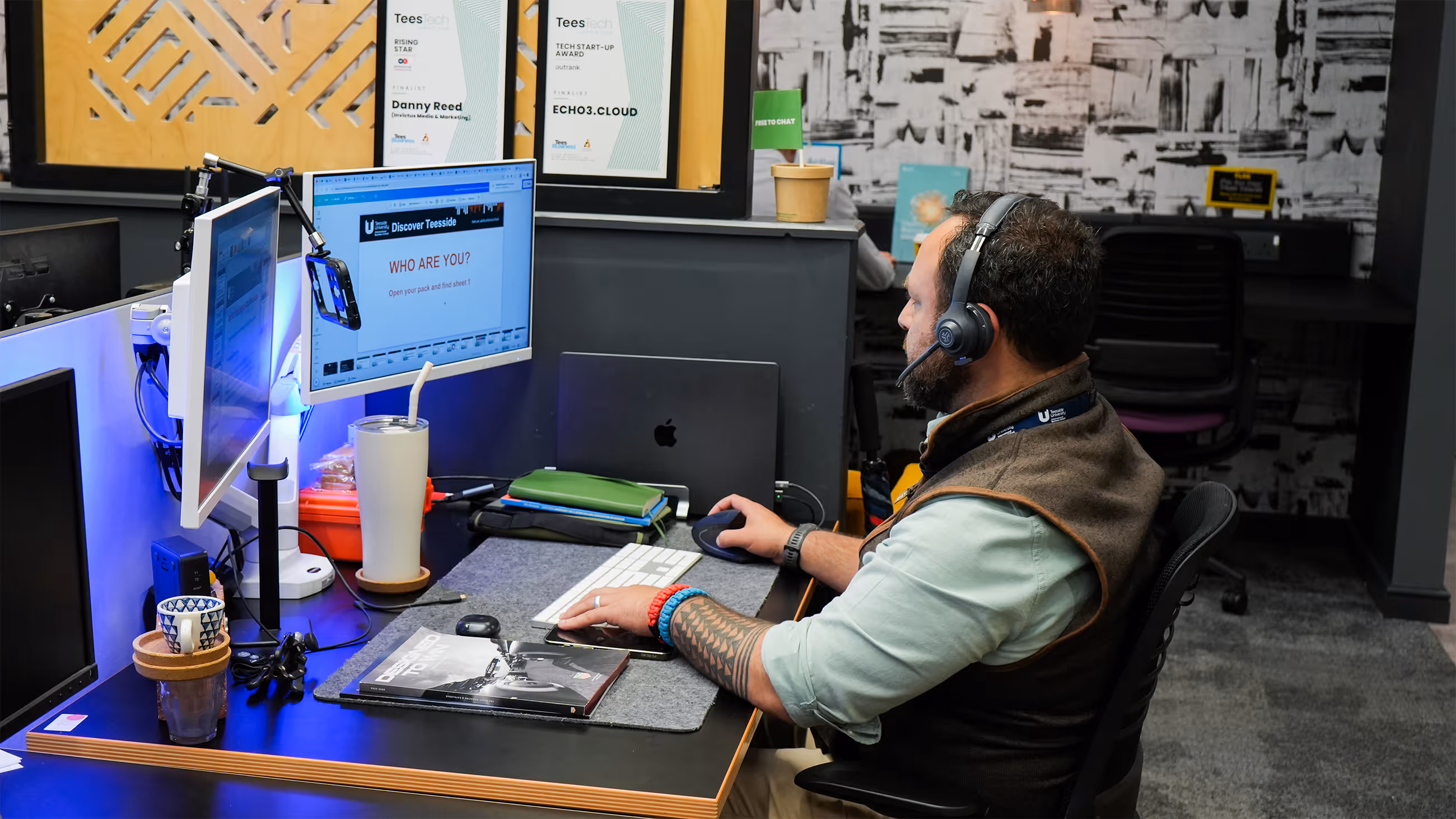 Man with headset using desktop computer with dual monitors at a modern office workstation.