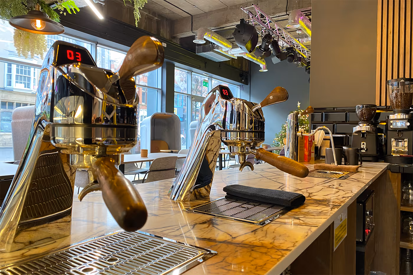 Coffee Mod Bar counter with two shiny espresso machines and coffee grinders on marble surface.