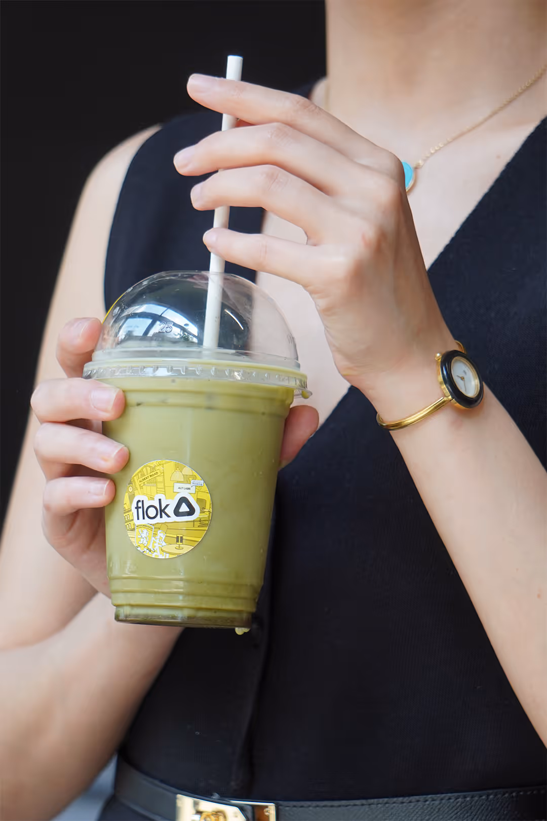 Person holding a plastic cup of iced green tea from flok cafe with a straw and clear dome lid.
