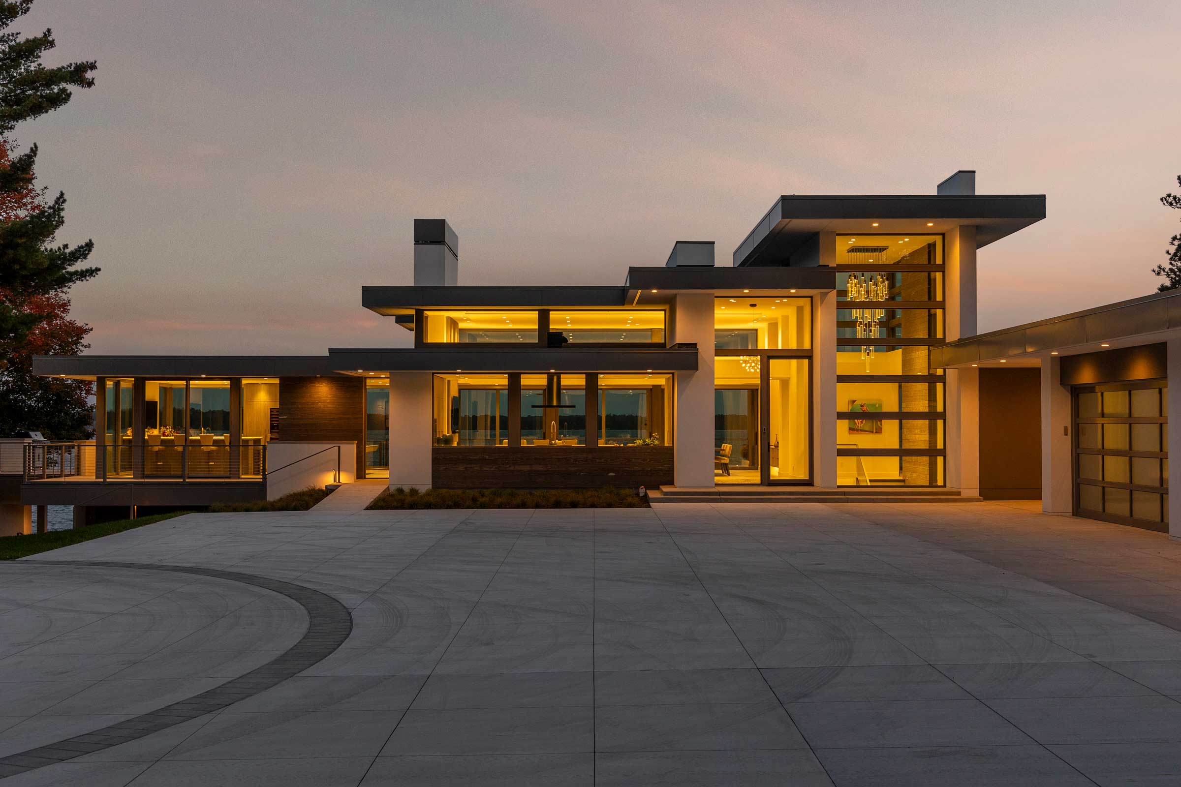 Night time photo of front of modern lake home with lights on