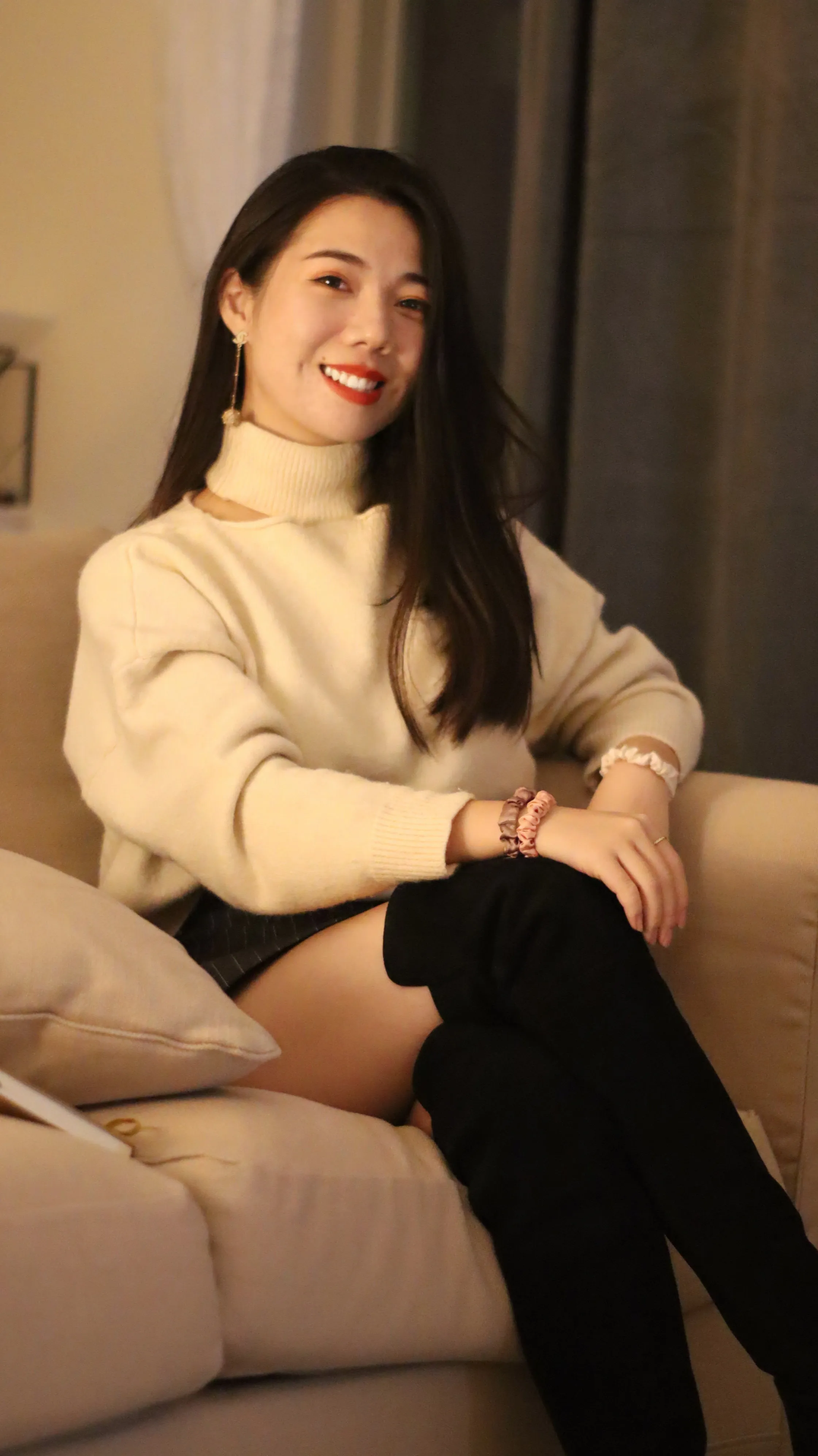 Grace, smiling, sits on the couch in a beige background 