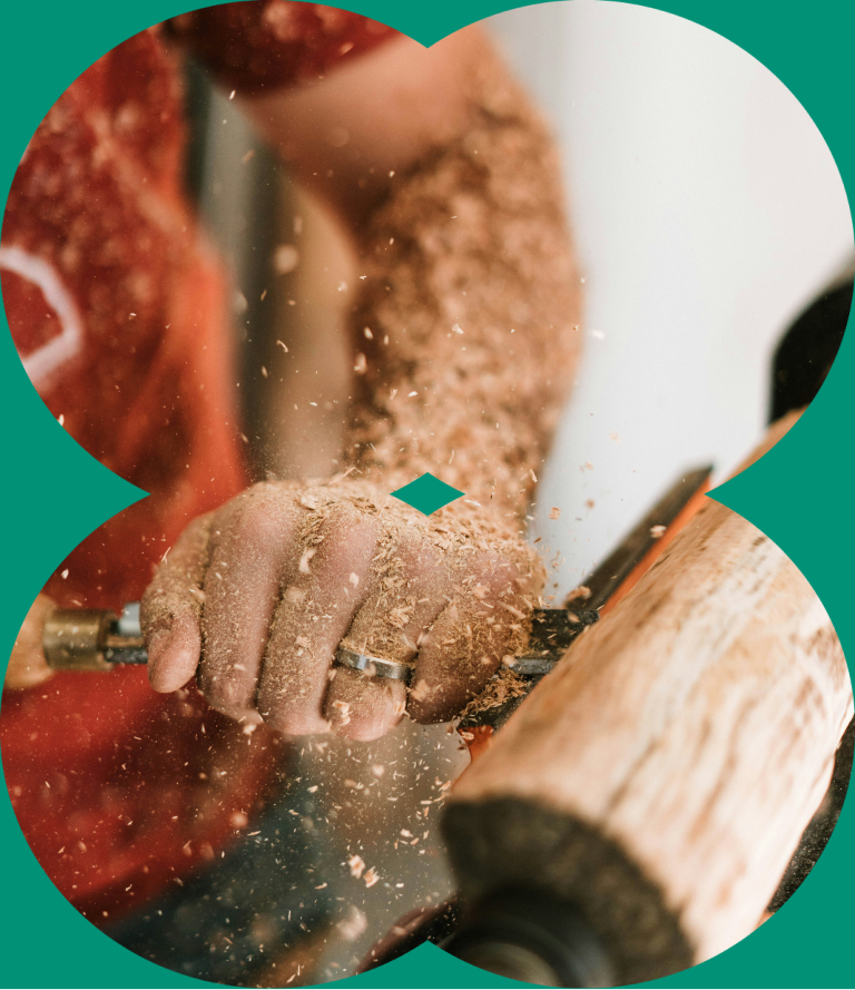 Close-up of a person carving wood on a lathe, with wood shavings flying around.