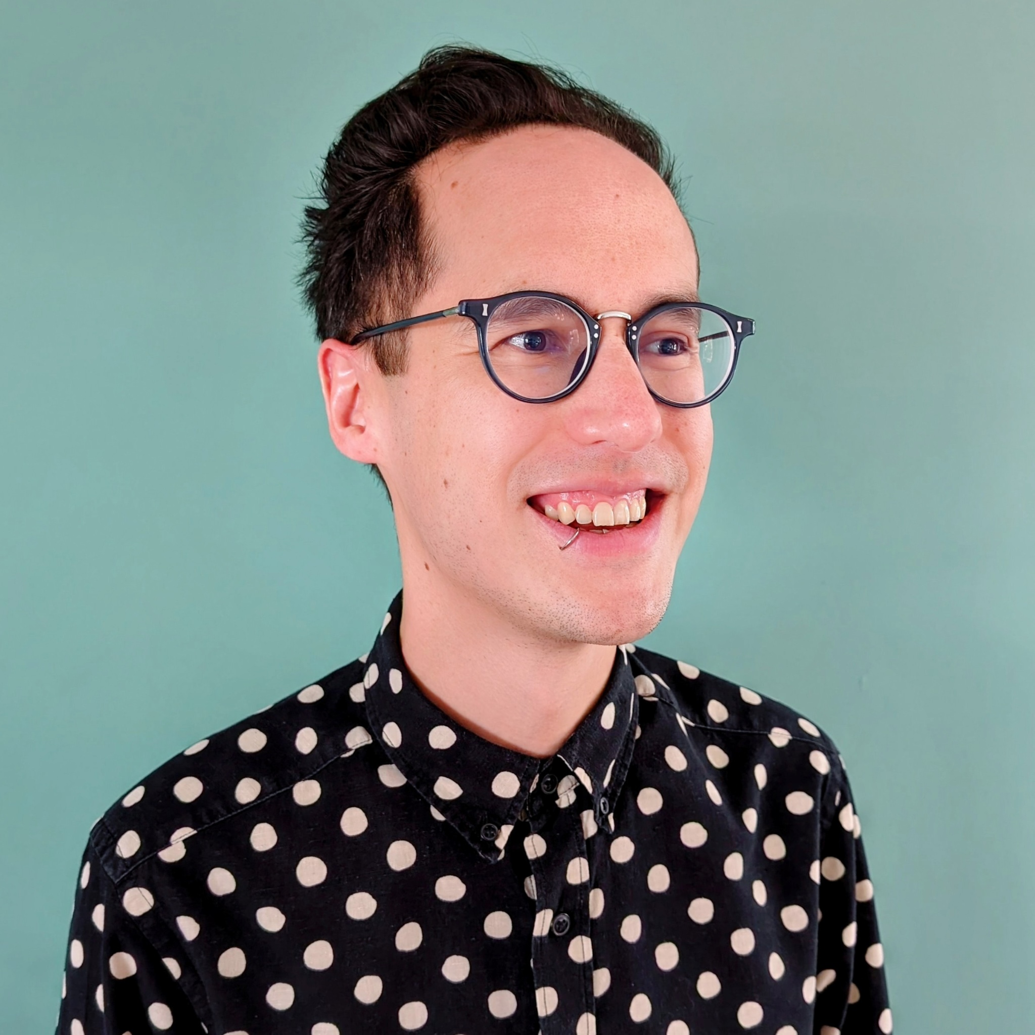 A photo of Jason Reed smiling and looking to the side, wearing a black and white polka dot shirt.
