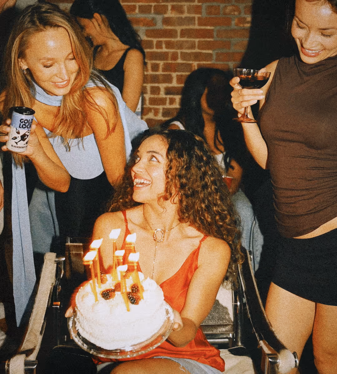 A group of ladies celebrate holding drinks and a cake.